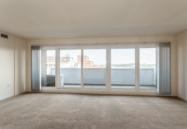 an empty living room with large windows and carpeting