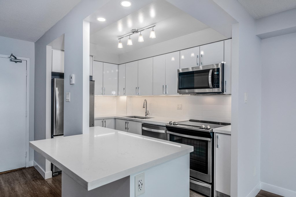 a white kitchen with white counter tops and stainless steel appliances
