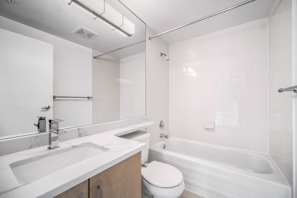 Image of a suite bathroom, which includes quartz countertops, stunning white tile, and chrome fixtures.