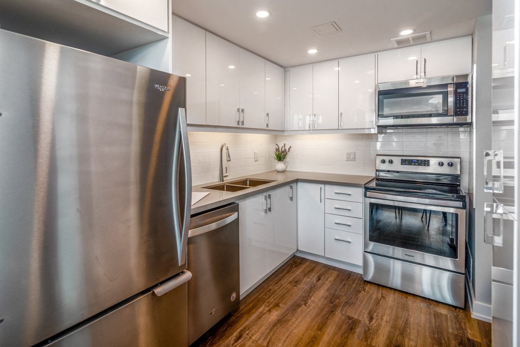 L-shaped kitchen with white glossy cabinets, refrigerator, and dishwasher.