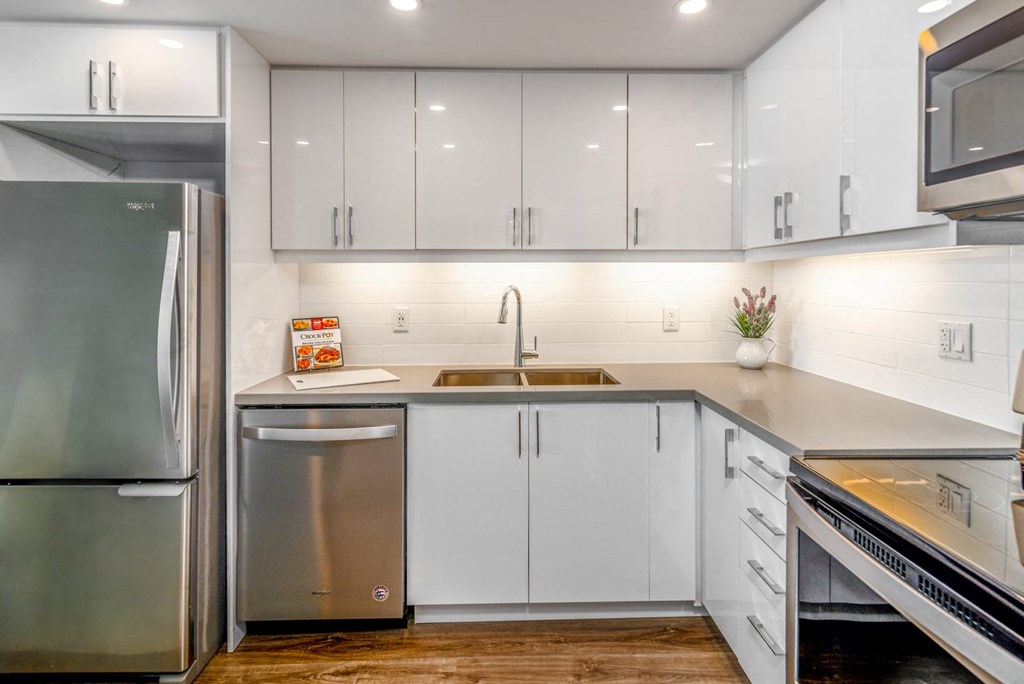 L-shaped kitchen with white glossy cabinets, refrigerator, and dishwasher.