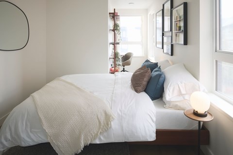 A bed with a white comforter and a white blanket is in the center of the image.