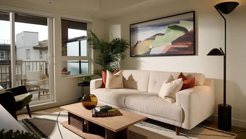 A living room with a white couch and a painting on the wall.