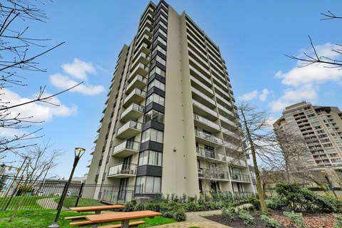 A tall residential building with balconies and a park in front.