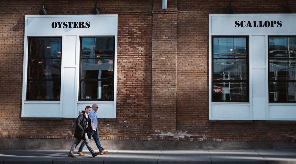 two people walking down the street in front of a brick building