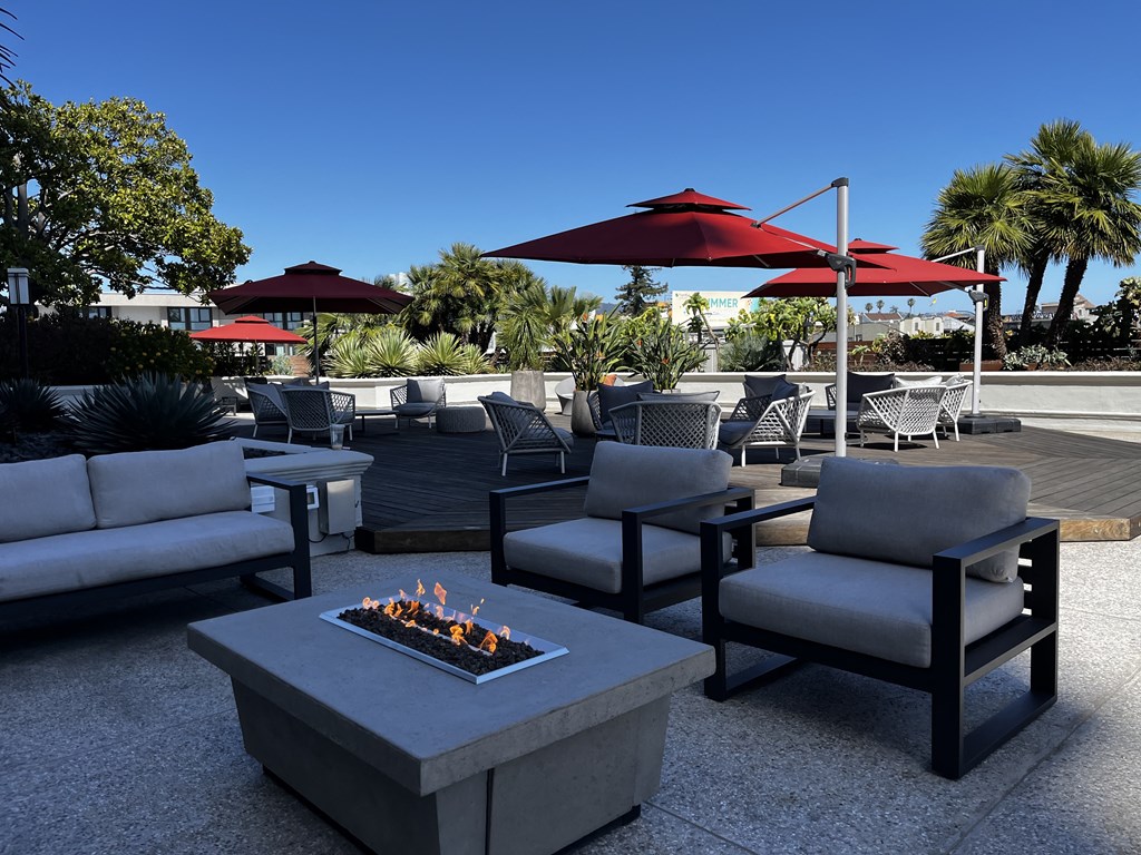 an outdoor patio with a fire pit and chairs and umbrellas