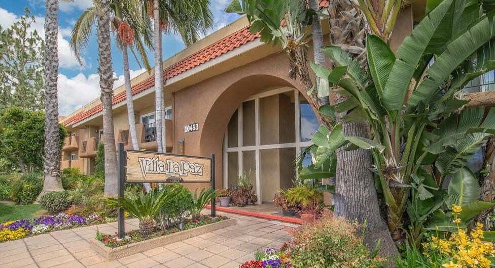 a building with a sign in front of it and palm trees at Villa La Paz Apartments, Bellflower, CA, 90706