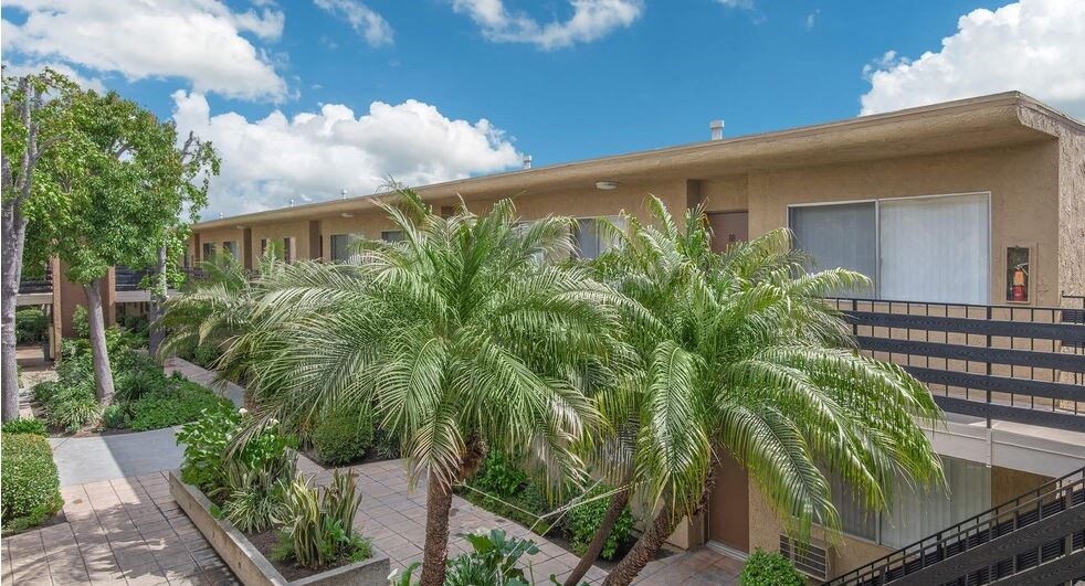 a building with palm trees in front of it at Villa La Paz Apartments, Bellflower, CA