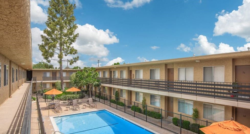 a hotel pool with umbrellas and tables and chairs at Villa La Paz Apartments, Bellflower, CA, 90706