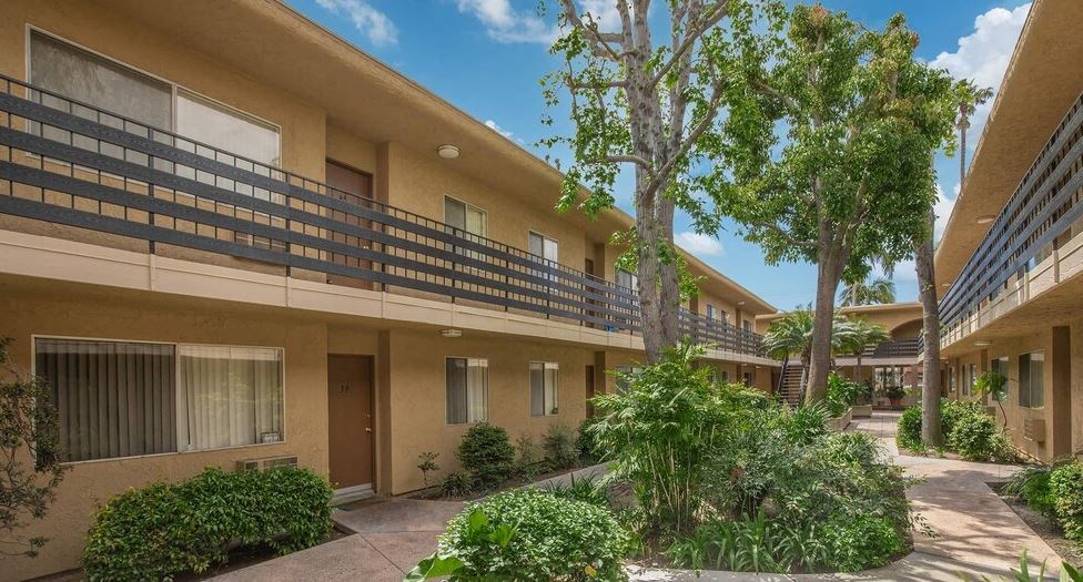 an apartment building with a courtyard and trees at Villa La Paz Apartments, Bellflower, California