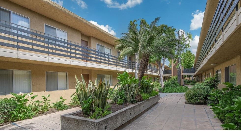 a building with palm trees in a courtyard at Villa La Paz Apartments, Bellflower, California