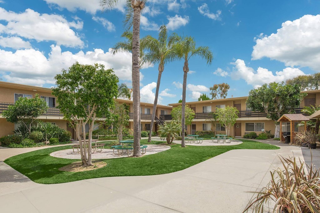 a courtyard with palm trees and a sidewalk in front of a building at Villa La Paz Apartments, California, 90706