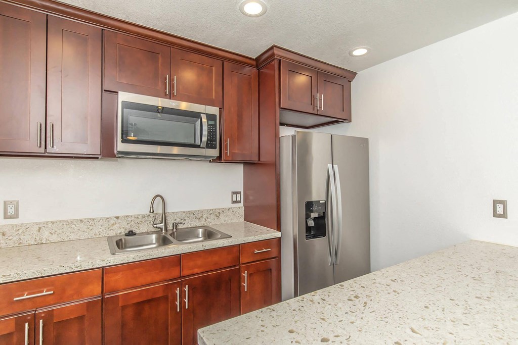 a kitchen with wooden cabinets and a stainless steel refrigerator at Villa La Paz Apartments, Bellflower, 90706