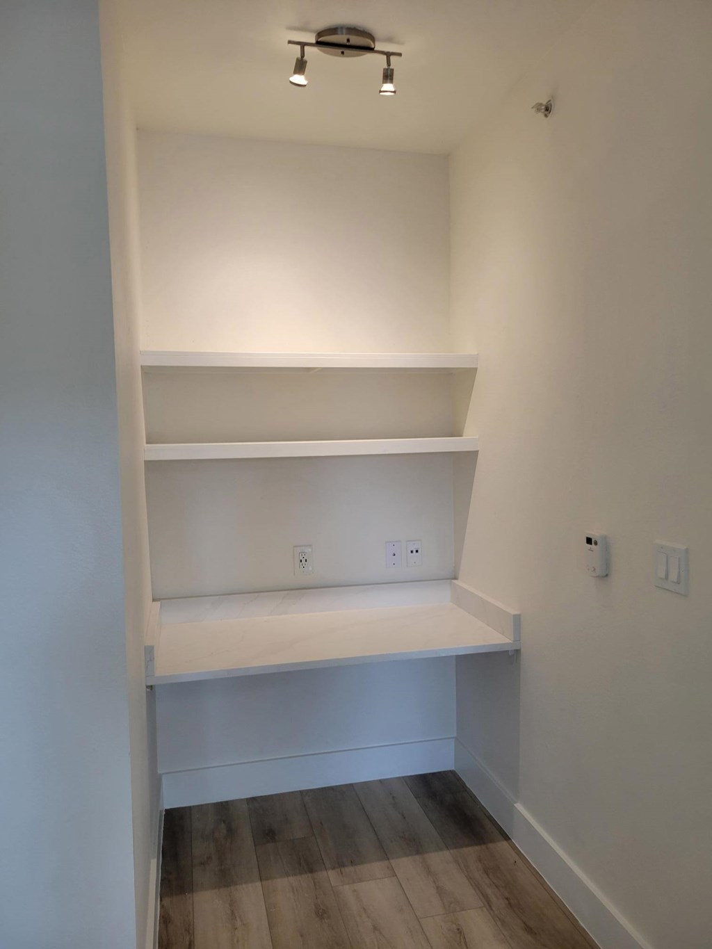 A white shelving unit with two shelves is in a room with white walls and wood flooring.