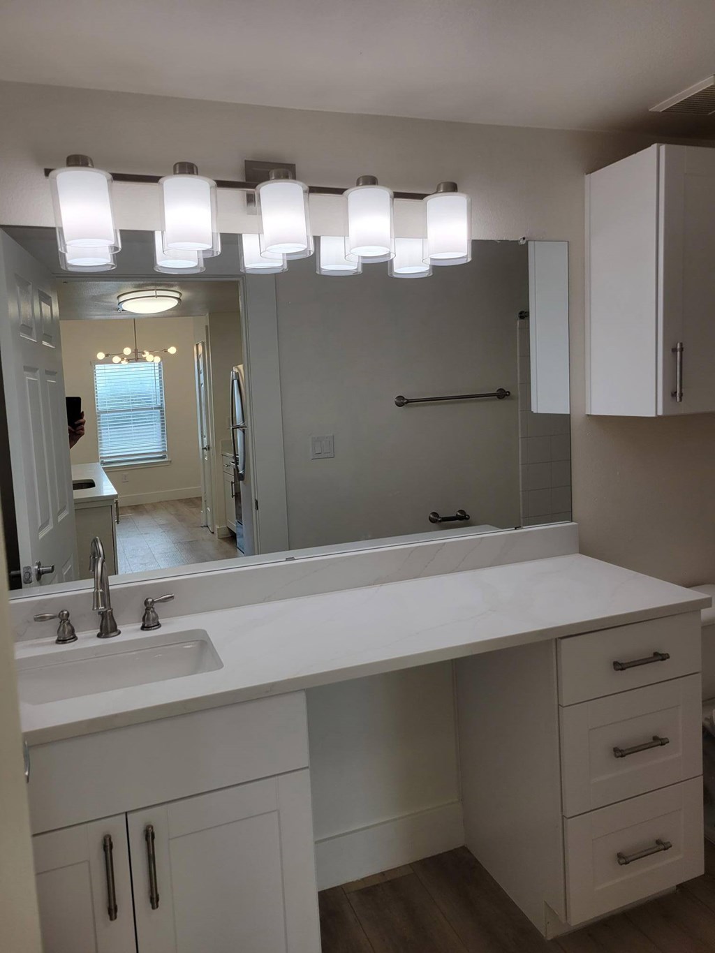 A bathroom with a white counter and a mirror with lights above it.