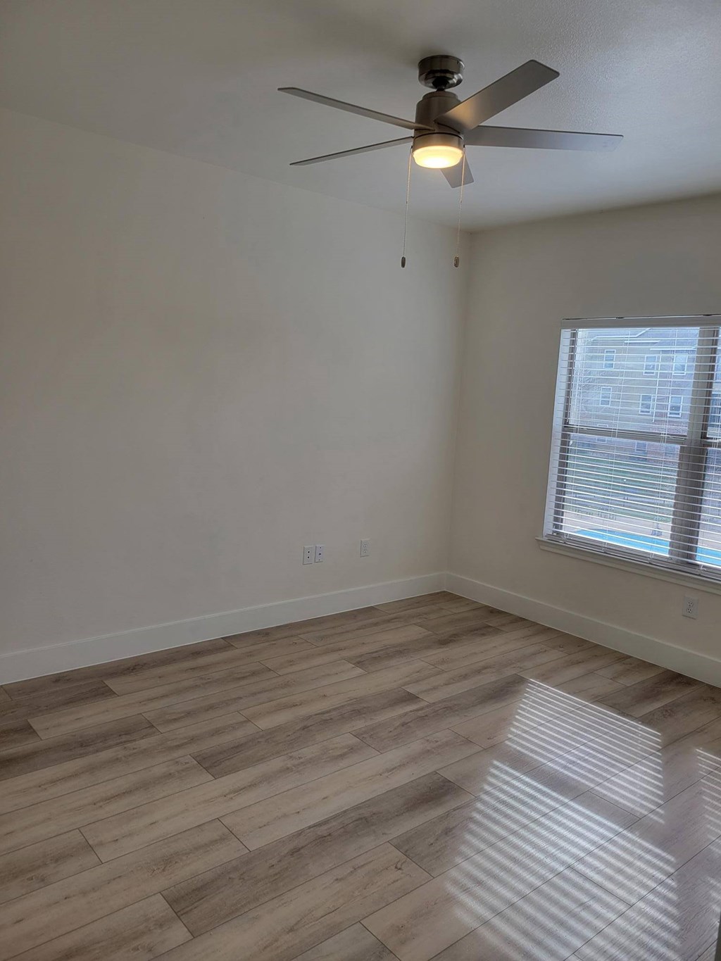 A room with a ceiling fan and a window with blinds.