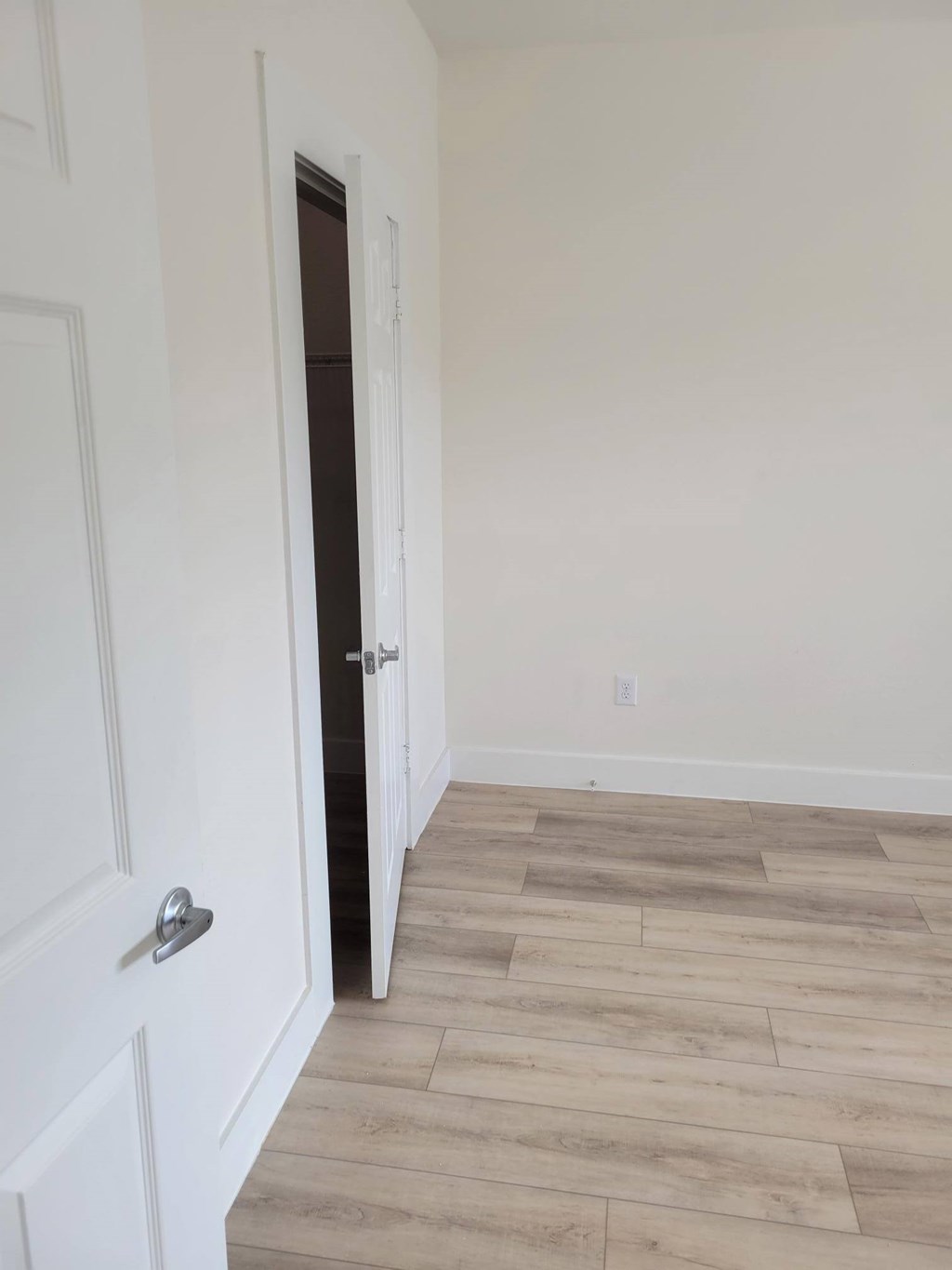 A white door with a silver handle is open to a room with wood flooring.