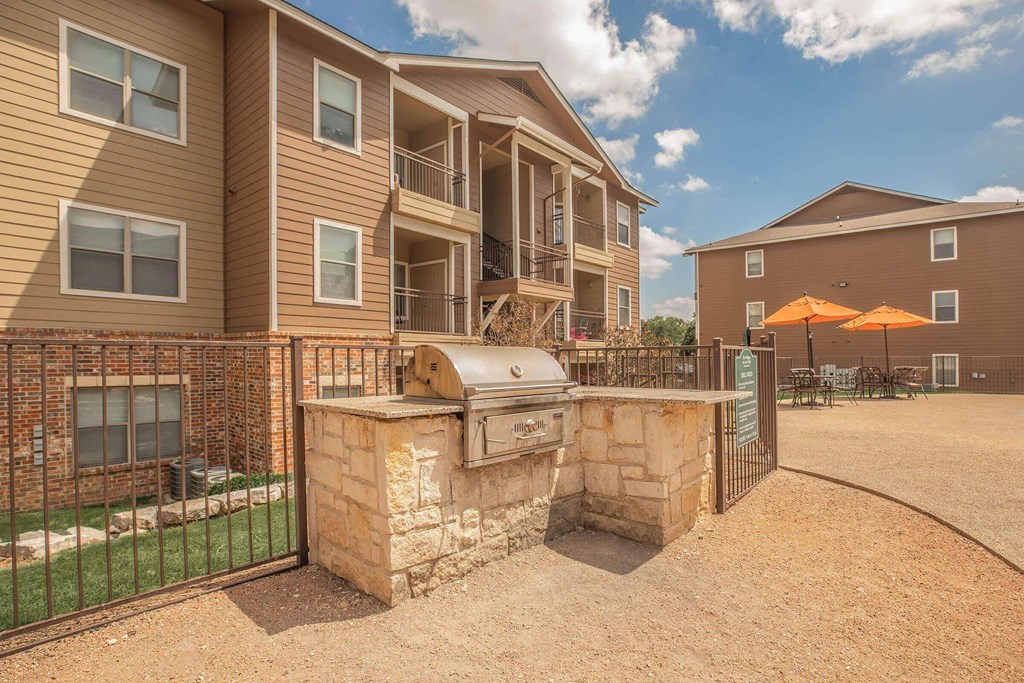 A sunny day at a residential complex with a fenced area and a stone structure at The Villages at Lost Creek Apartments, San Antonio, TX