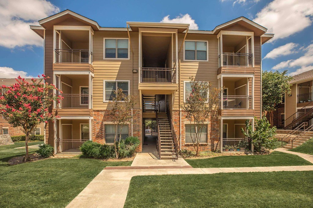 A large apartment building with a green lawn in front at The Villages at Lost Creek Apartments, San Antonio, Texas