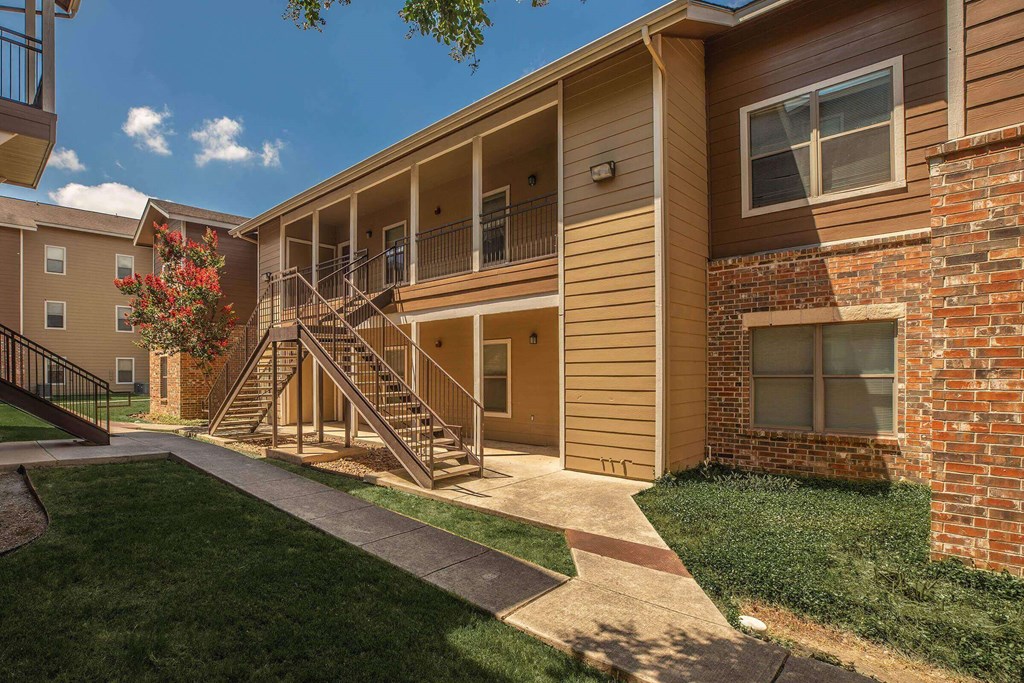 A sunny day at a brick apartment complex with a red flower in bloom at The Villages at Lost Creek Apartments, San Antonio, TX, 78247