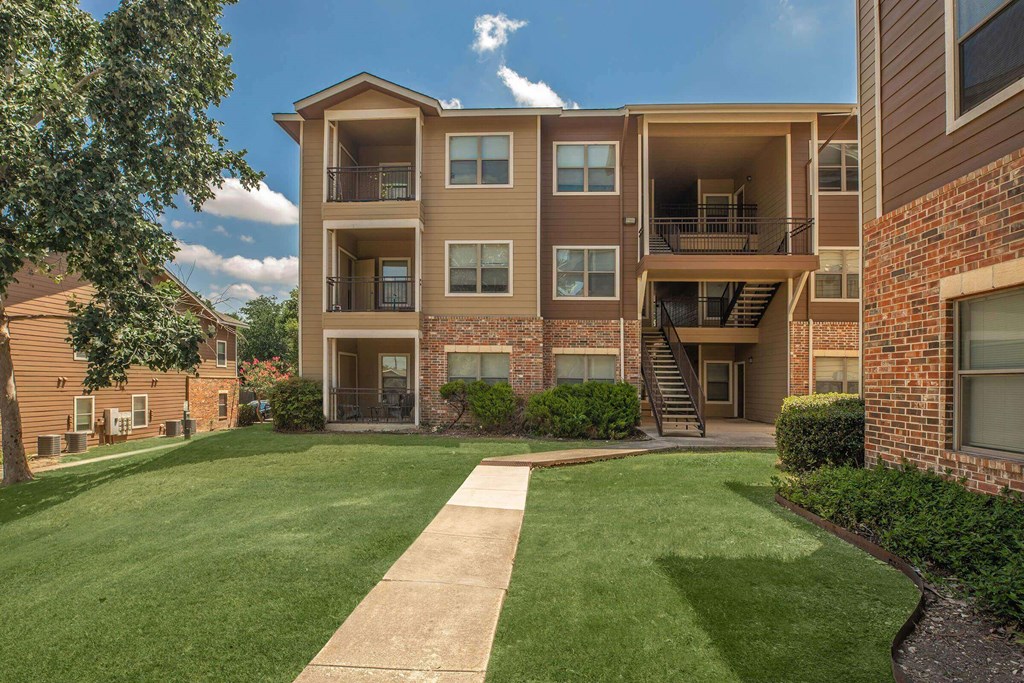 A large apartment complex with a green lawn in front at The Villages at Lost Creek Apartments, Texas