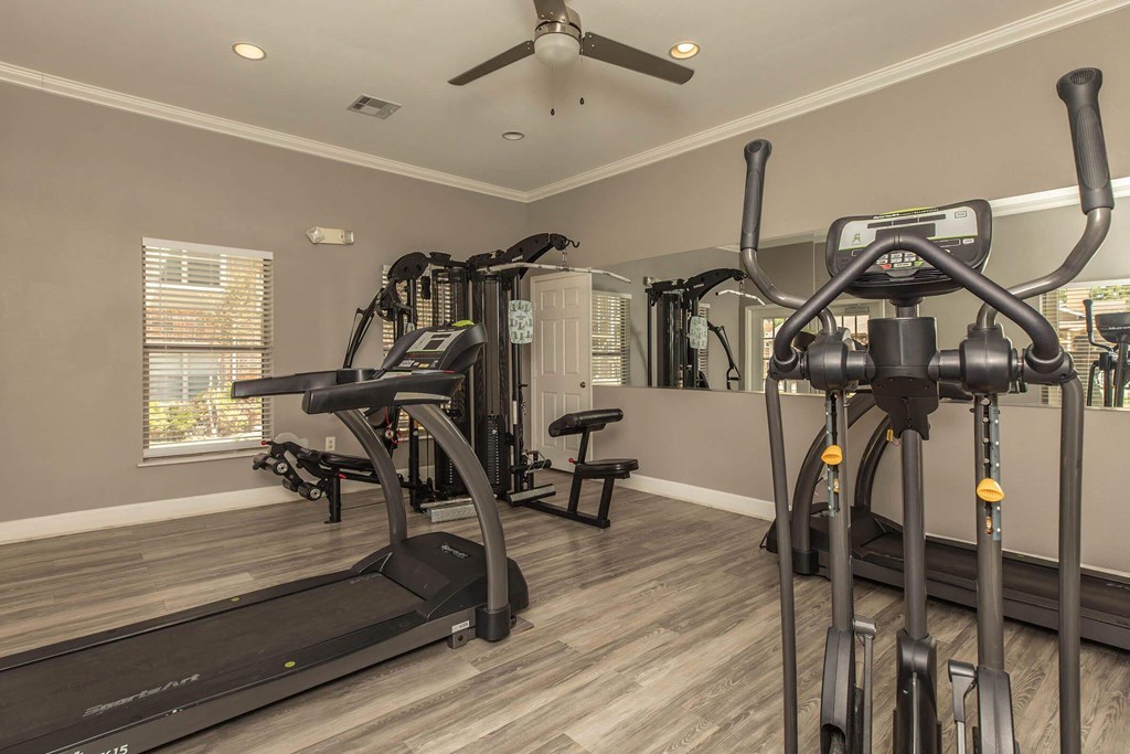 A spacious home gym with a treadmill, elliptical trainer, and a bench at The Villages at Lost Creek Apartments, San Antonio, 78247