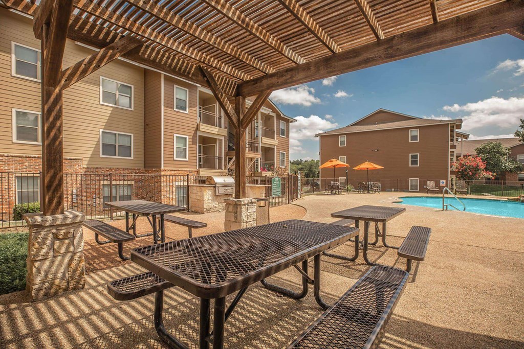 A patio with tables and benches under a wooden pergola at The Villages at Lost Creek Apartments, Texas