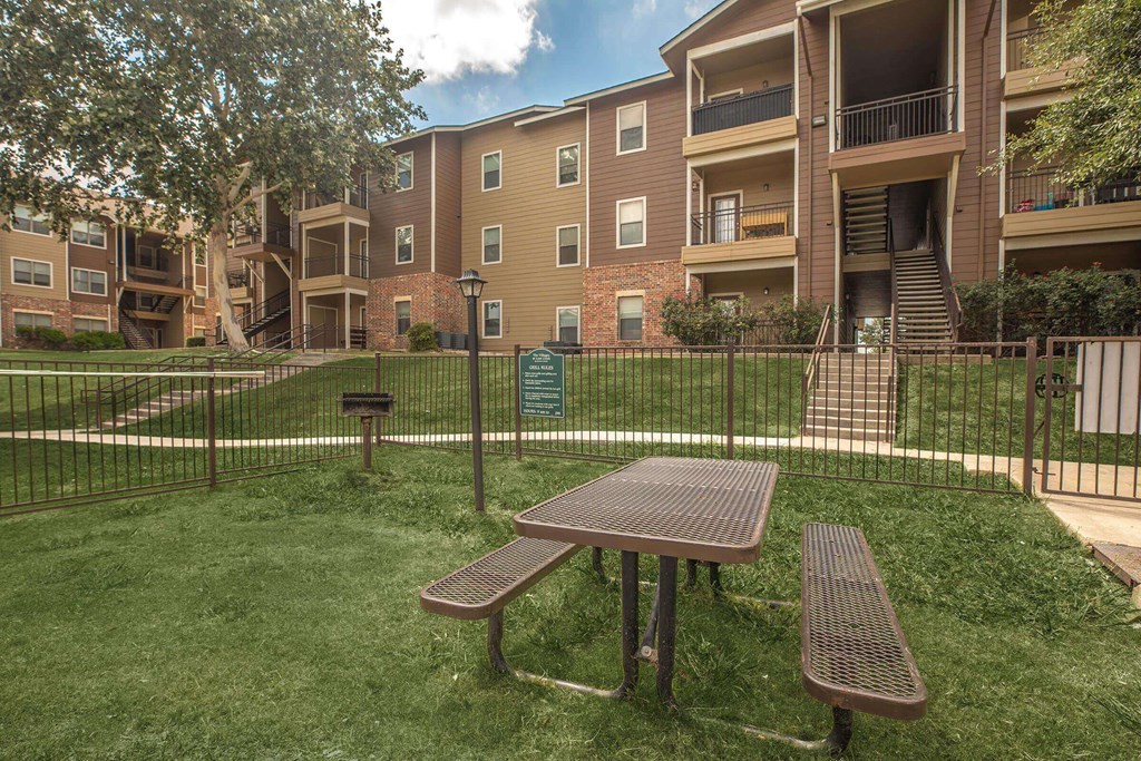 A picnic table and two benches are in front of a fence and apartment building at The Villages at Lost Creek Apartments, San Antonio, 78247