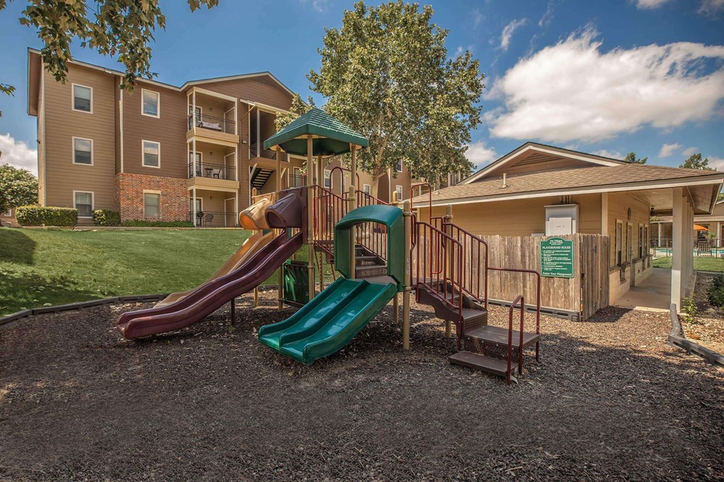 A playground with a green slide and a red slide in front of a building. A playground with a green slide and a red slide in front of a building at The Villages at Lost Creek Apartments, San Antonio, TX