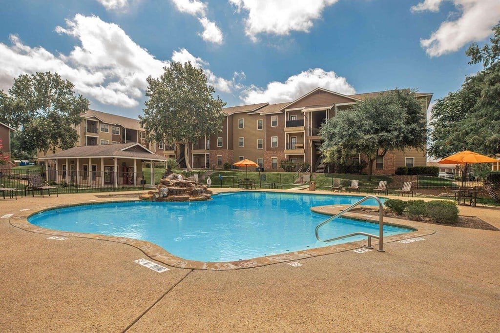 A large swimming pool surrounded by a fence and trees with apartment buildings in the background at The Villages at Lost Creek Apartments, Texas, 78247