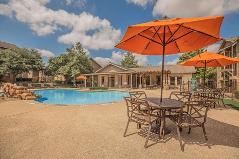 A large orange umbrella is in the foreground of a pool area.