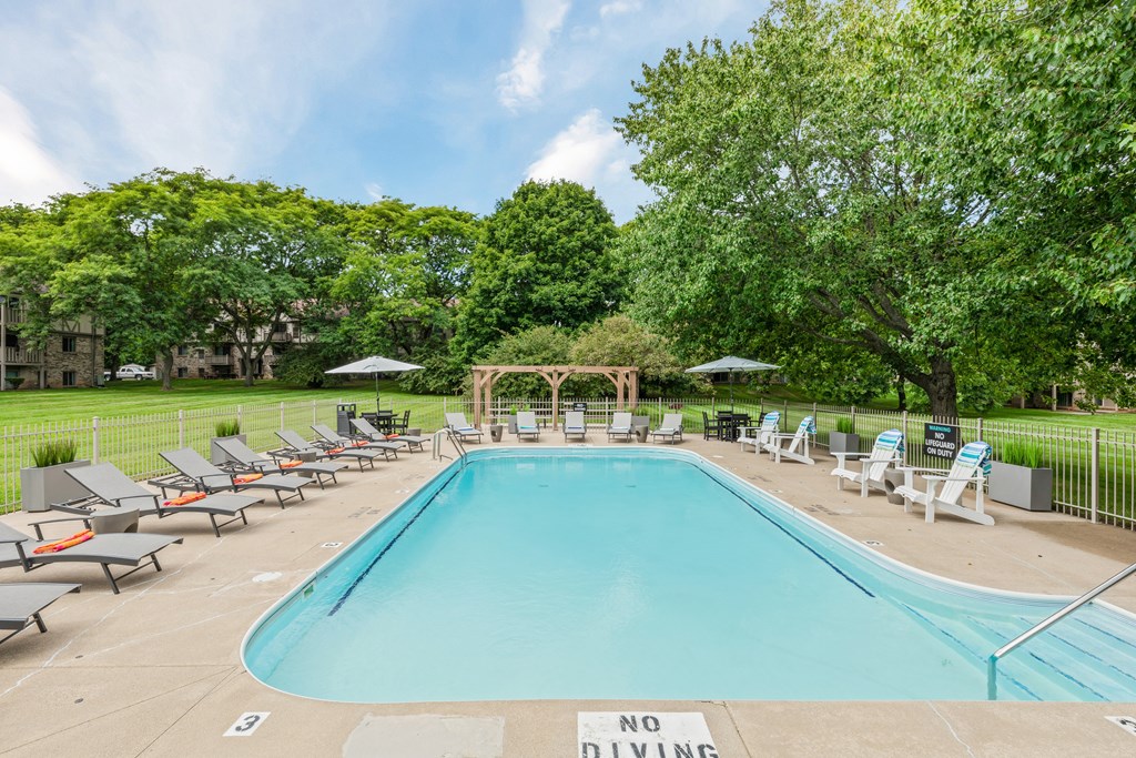 A pool surrounded by lawn chairs and trees with a sign that says no diving.