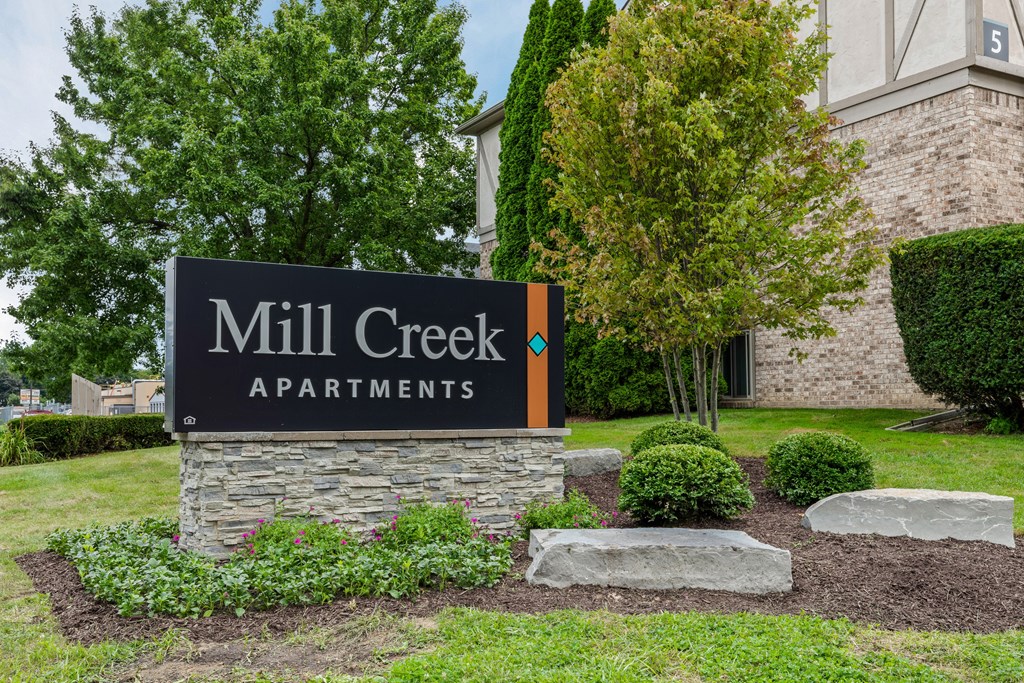 A sign for Mill Creek Apartments is displayed in front of a building.