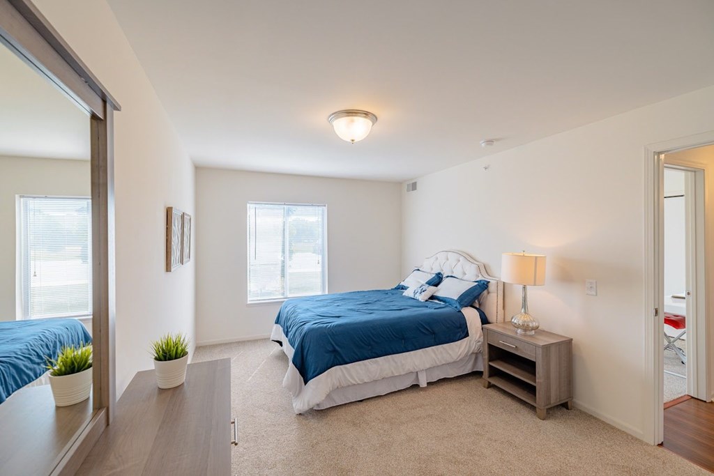 A bedroom with a bed, nightstand, and a plant.