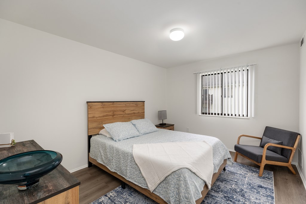 A bedroom with a bed, chair, and window.