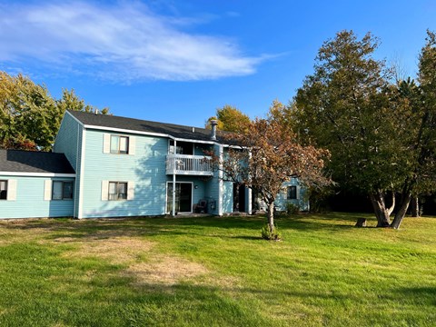 A blue house with a white fence and a tree in front.