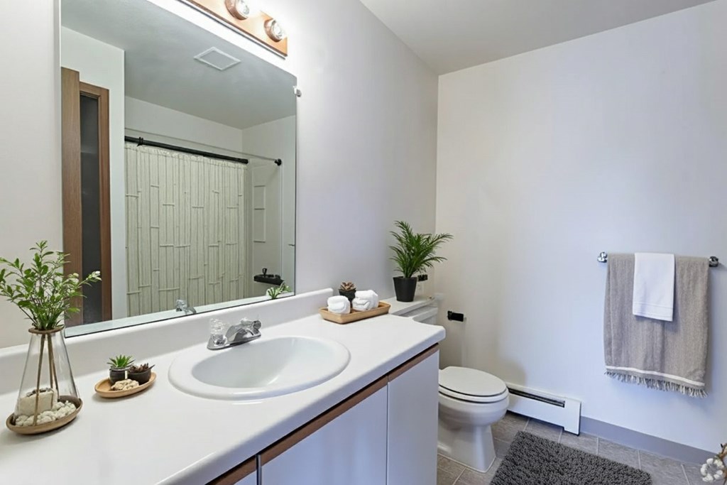 A white bathroom with a sink, mirror, toilet, and a plant.