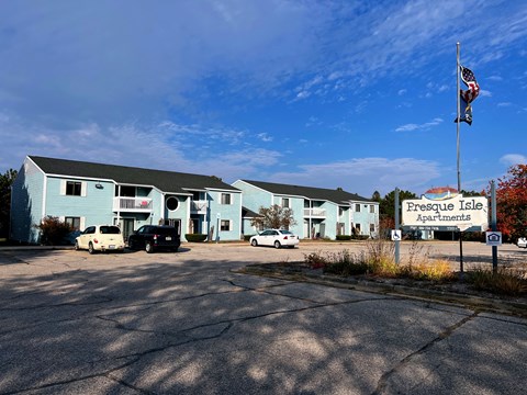 A parking lot in front of a blue building with a sign that says Presque Isle Apartments.