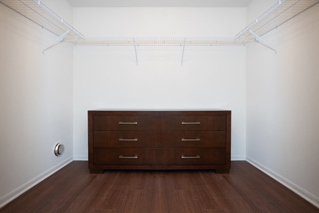 A brown dresser is in a white room with a white ceiling and a white wall.