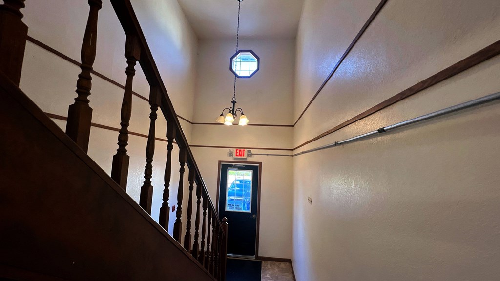 a hallway with a staircase and a door with a chandelier