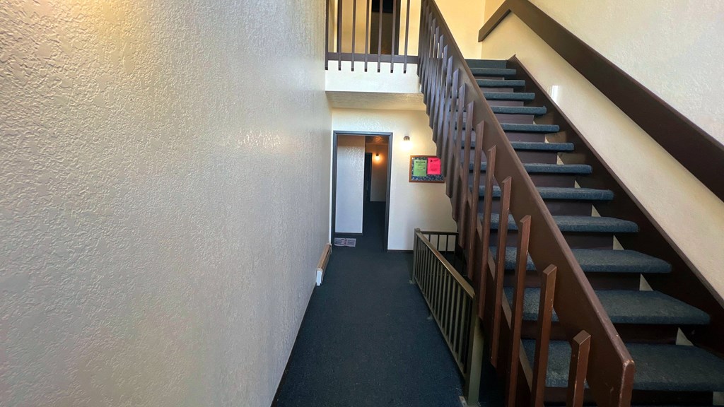 a long hallway with stairs and a door to a hallway with a staircase