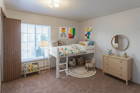 A child's bedroom with a white bed, a wooden dresser, and a round mirror on the wall.