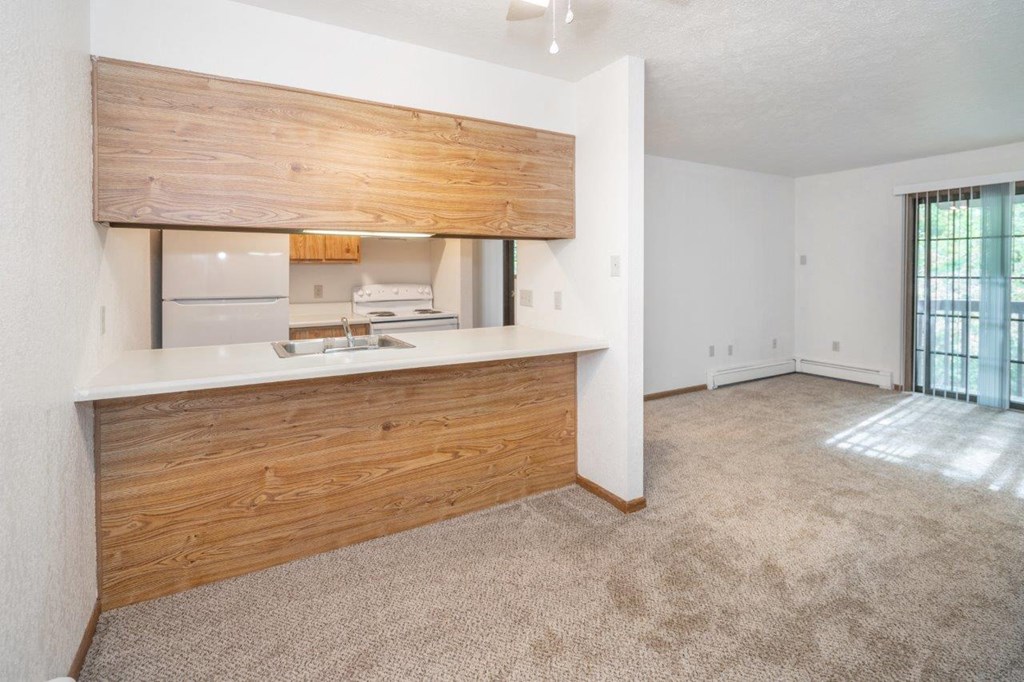 an empty living room with a kitchen and a window