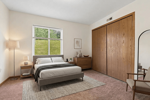 A bedroom with a large bed, a nightstand with a lamp, a chair, and a wooden wardrobe.