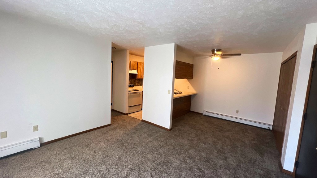 an empty living room with a kitchen in the corner