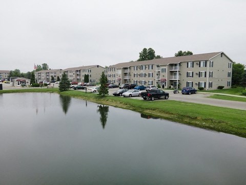 a body of water in front of an apartment building with cars parked in the lot