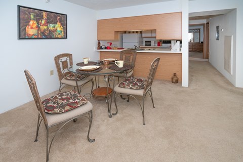 a dining area with a table and chairs and a kitchen in the background