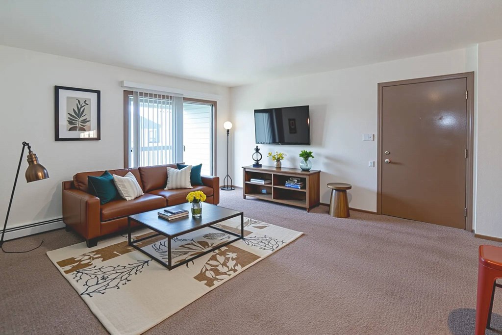 A living room with a brown couch, a coffee table, and a flat screen TV mounted on the wall.