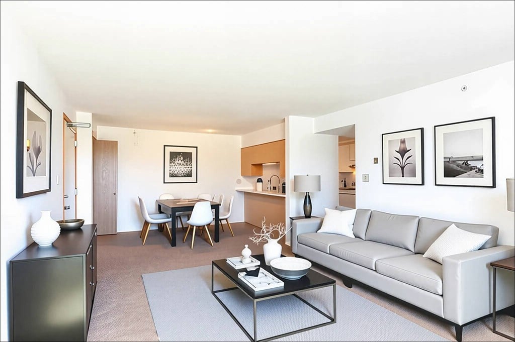 A modern living room with a grey couch, a glass coffee table, and a dining table with chairs.
