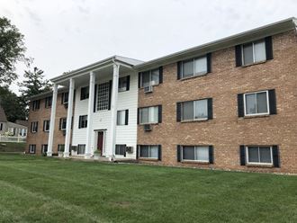 a large brick building with white siding and a large grassy area in front of it